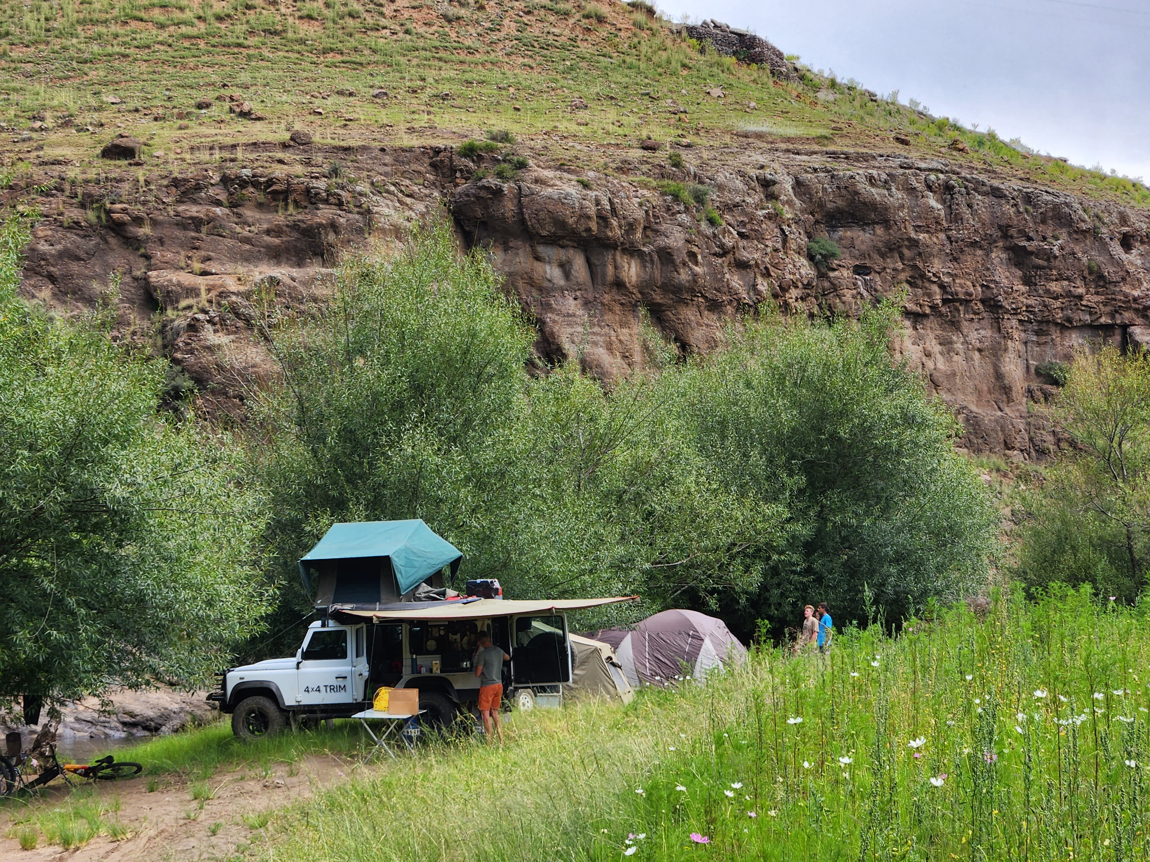 A back-up vehicle and tents at a wild camping spot beside a river in Lesotho